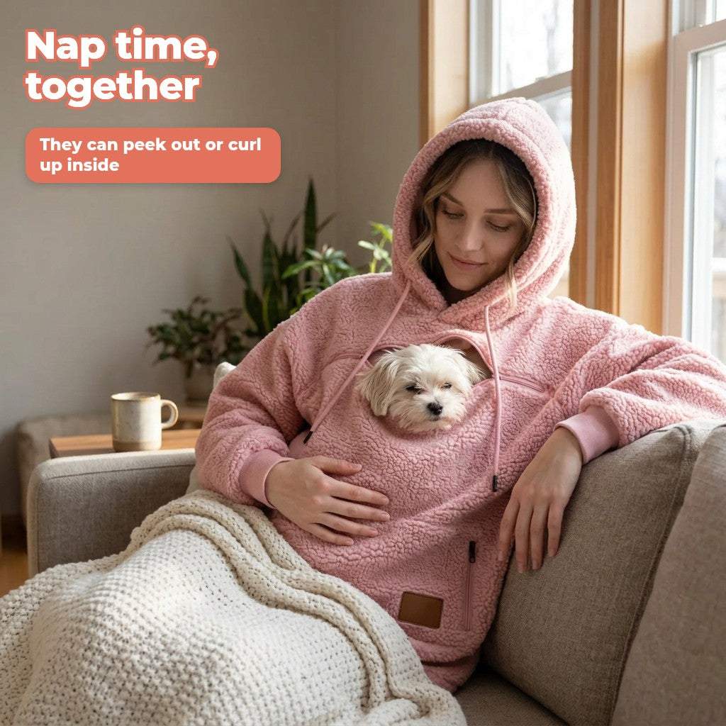 Pink sherpa pet pouch hoodie with a Maltese peeking out on the sofa